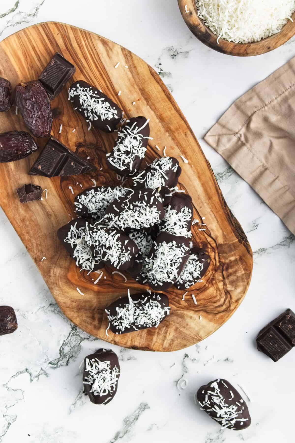 A pile of chocolate covered dates on a wooden board.