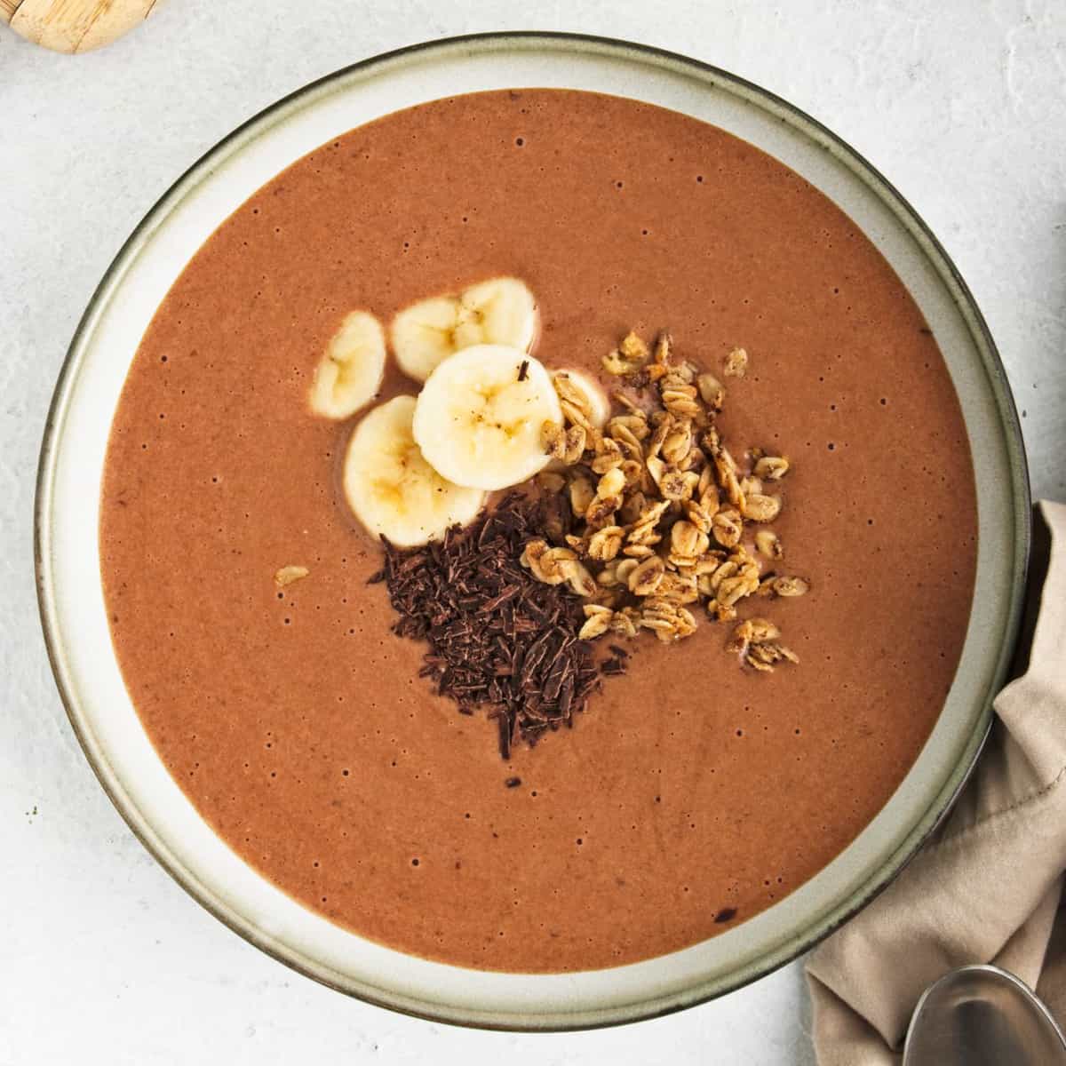 Chocolate smoothie in a bowl topped with banana, grated chocolate and granola.