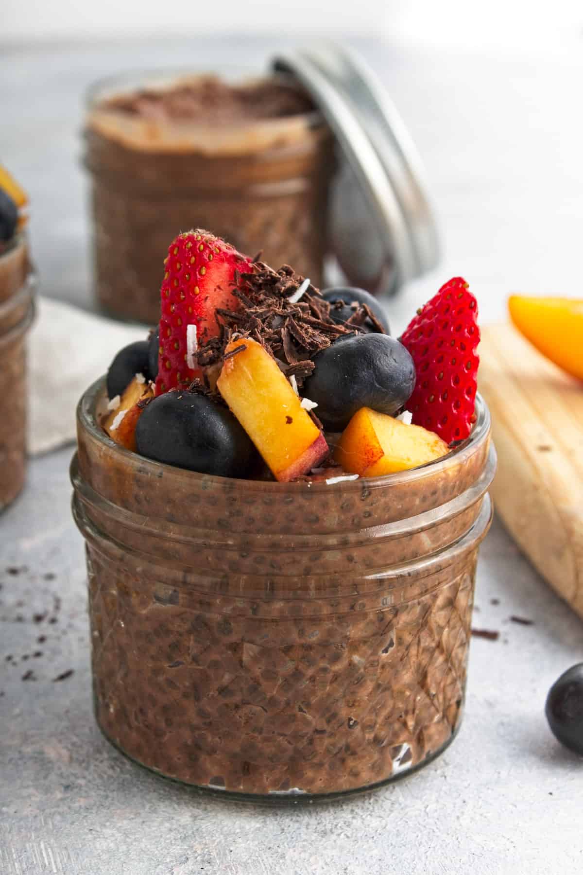 A patterned mason jar full of chia pudding garnished with peach, blueberry, strawberry and grated chocolate.