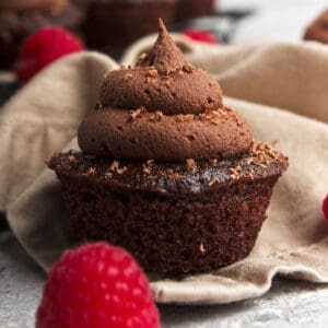 A vegan chocolate cupcake topped with ganache, shaved chocolate and raspberries.