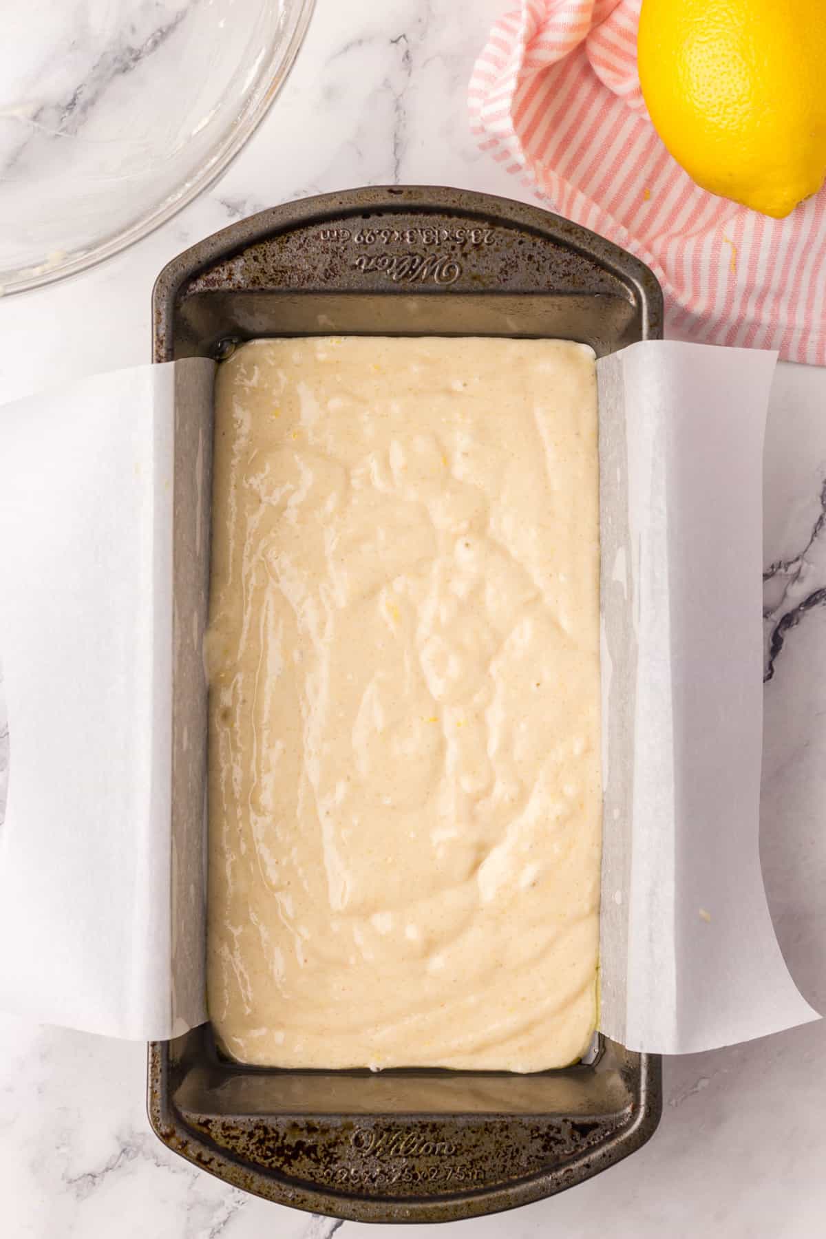 A lined loaf pan with lemon cake batter in.