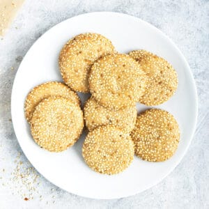 A pile of tahini cookies covered in sesame seeds on a white plate.