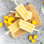 Creamy mango popsicles on a wooden board.