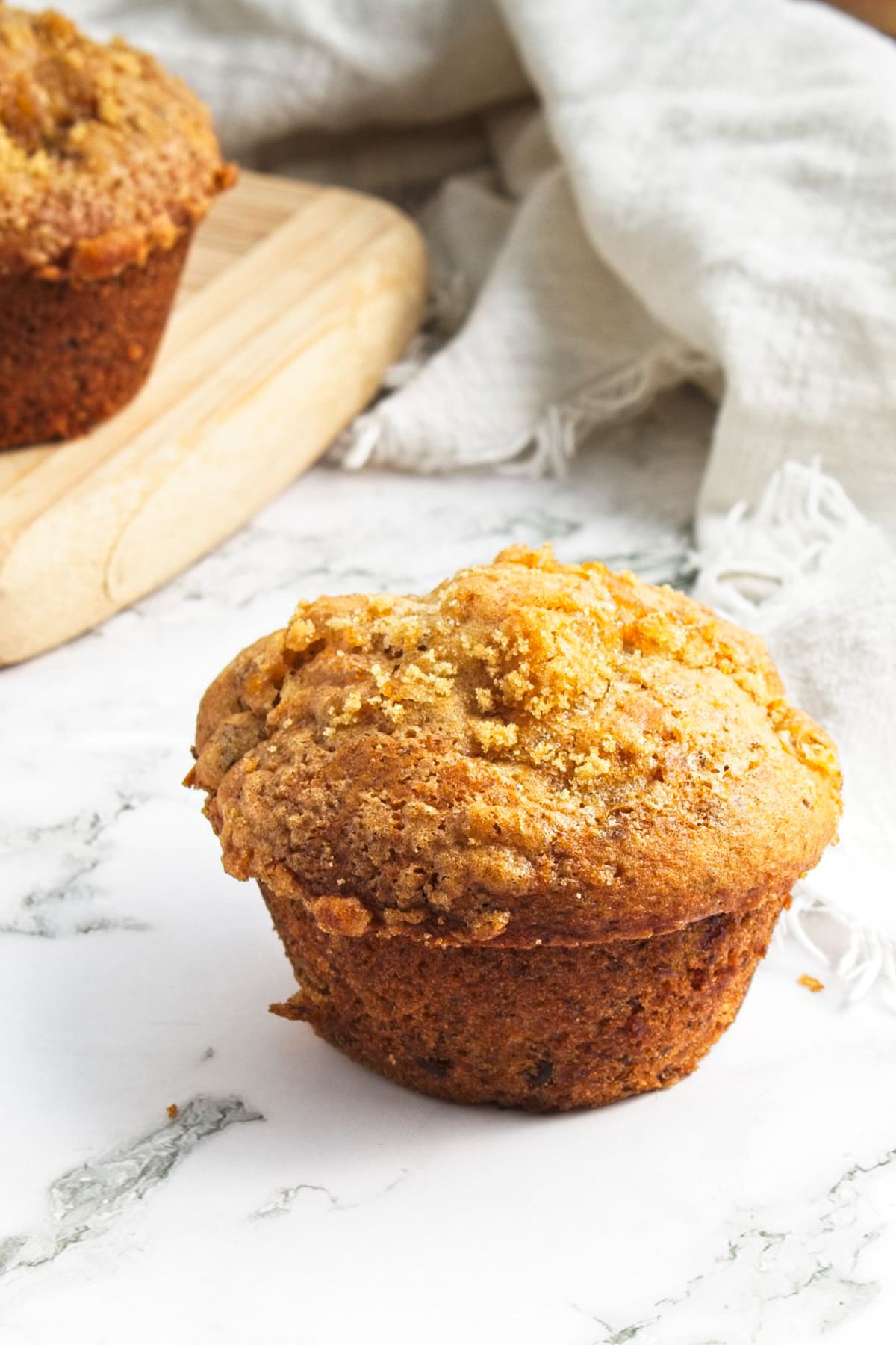 A fluffy and golden peach muffin on a marble worktop.