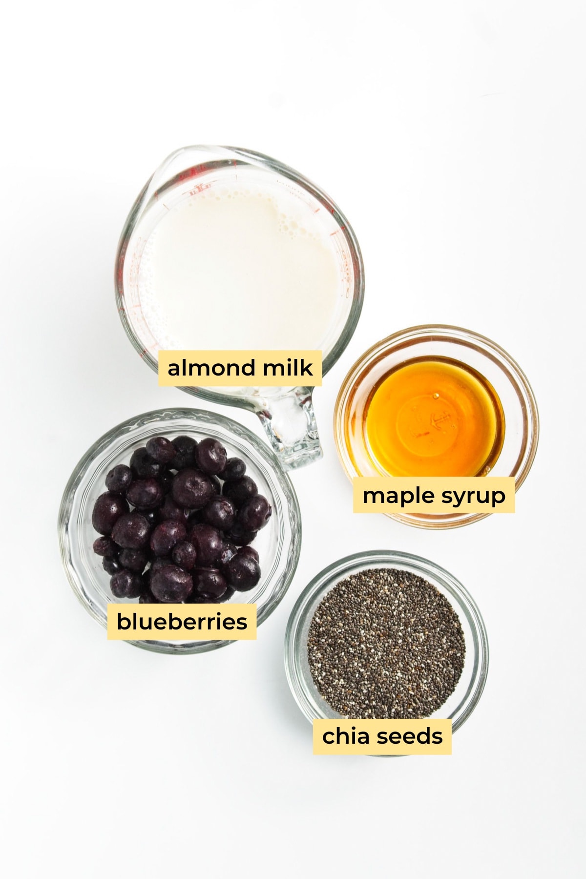 Ingredients in glass bowls: maple syrup, blueberries, chia seeds and almond milk.