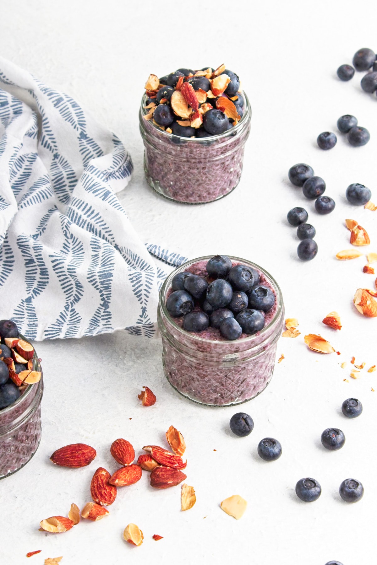 Jars of blueberry chia seed pudding with topping ingredients scattered around.