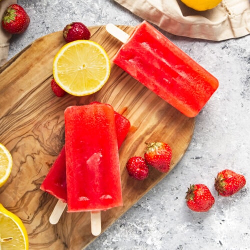 Three strawberry lemonade popsicles on a wooden board.