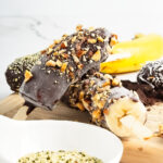 Two chocolate and nut covered bananas in a stack.