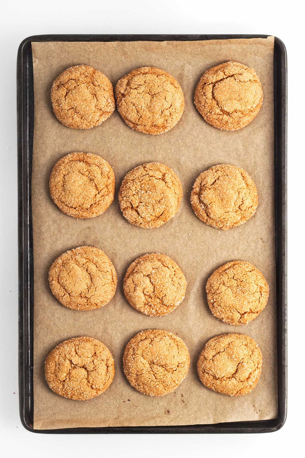 Twelve freshly baked ginger cookies on a lined baking sheet.
